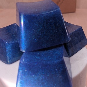 May include: Four blue square-shaped keycaps with a glittery finish.