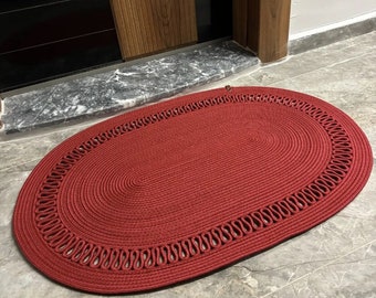 Könnte beinhalten: Roter ovaler Fußabtreter mit geflochtenem Design und dekorativem Rand. Der Fußabtreter ist aus gewebtem Material gefertigt und hat eine strukturierte Oberfläche.