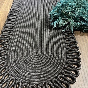 May include: Black oval braided rug with a decorative rope border. The rug is made of thick, woven rope and has a fringed edge.