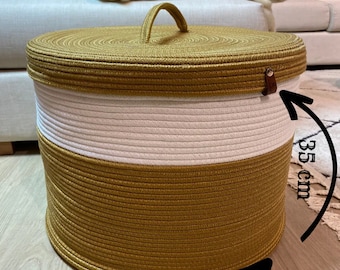 May include: A large, round, woven storage basket with a lid and a handle. The basket is made of natural rope and has a white and gold color scheme. The basket measures 17.7 inches in diameter and 17.7 inches in height.