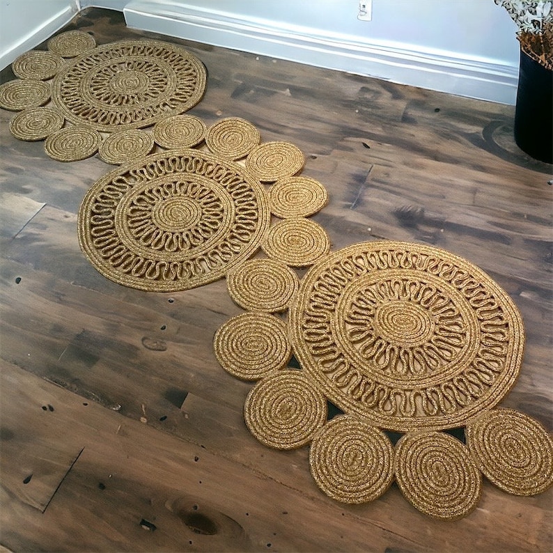 Puede incluir: Un conjunto de tres alfombras redondas de yute de color dorado con un patr&oacute;n circular. Las alfombras est&aacute;n dispuestas en fila, con la alfombra m&aacute;s grande en la parte posterior y la m&aacute;s peque&ntilde;a en la parte delantera.
