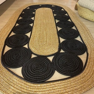 May include: Oval jute rug with a natural tan center and border, featuring a pattern of black circular accents. The rug's design adds a modern touch to any room. The rug is approximately 60 inches long and 36 inches wide.