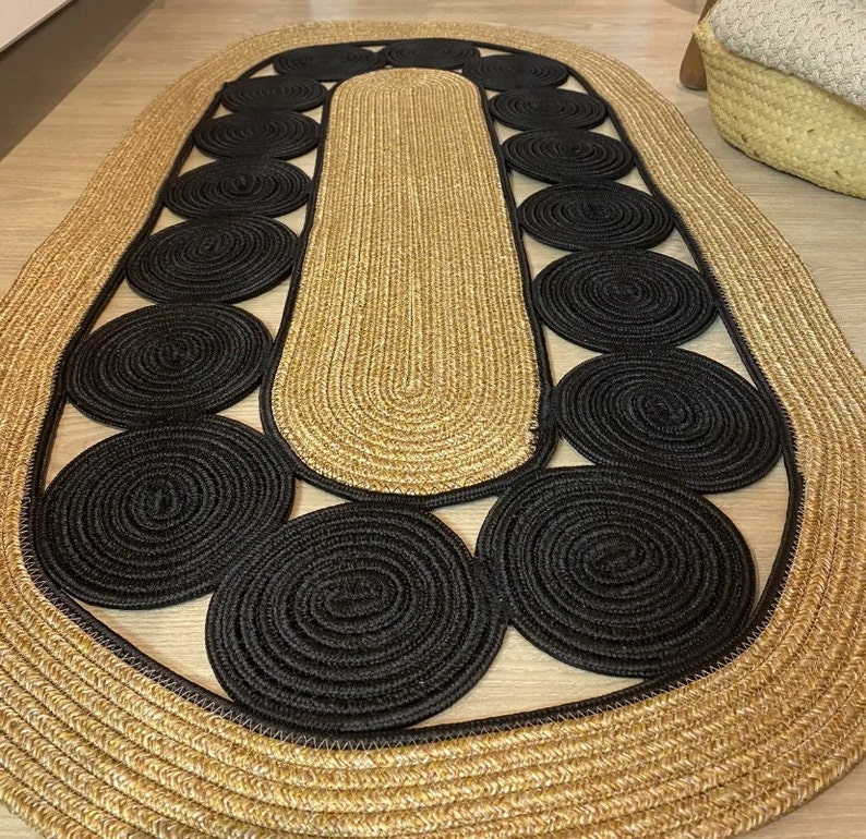 May include: Oval jute rug with a natural tan center and border, featuring a pattern of black circular accents. The rug's design adds a modern touch to any room. The rug is approximately 60 inches long and 36 inches wide.