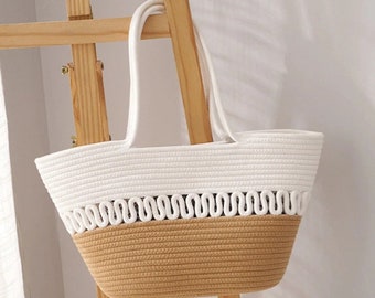 Pode incluir: Uma bolsa tote de corda branca e bege com um design tecido. A bolsa tem duas alças e uma abertura larga.