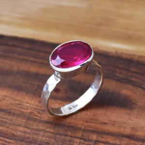 Op de afbeelding: Een zilveren ring met een grote, ovale, roze edelsteen gezet in een bezel setting. De ringband is gehamerd en heeft een textuur.