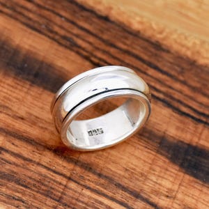 Könnte beinhalten: Ein silberner Drehring mit einer glatten, abgerundeten Oberfläche und einer schwarzen Linie am Rand. Der Ring ist innen mit "925" gekennzeichnet.