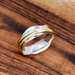 Puede incluir: Un anillo de plata y oro con un diseño único y retorcido. El anillo está hecho de dos bandas, una de plata y otra de oro, que están entrelazadas y retorcidas.