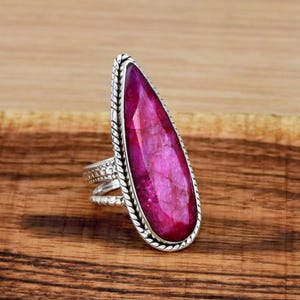 May include: A silver ring featuring a large, pink, faceted gemstone set in a twisted silver band.