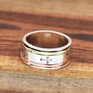 May include: A silver, gold, and copper spinning ring with a cross design. The ring is made of three bands that spin independently.