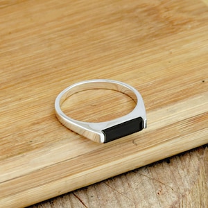 Könnte beinhalten: Ein silberner Ring mit einem schwarzen rechteckigen Stein, der in die Band eingefasst ist.