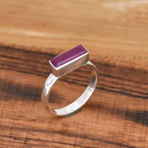 Może przedstawiać: Srebrny pierścionek z prostokątnym, fioletowym kamieniem szlachetnym osadzonym w obrączce.