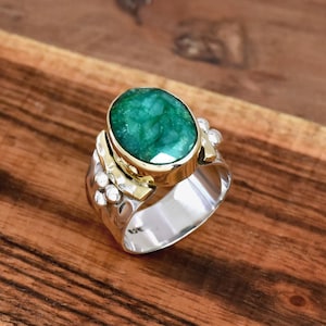 Pode incluir: Um anel de prata e ouro com uma grande esmeralda oval. O anel tem uma banda texturizada e um design decorativo.