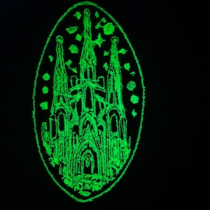 May include: A green glow-in-the-dark embroidered patch of a cathedral with a pointed roof and multiple towers. The patch is oval shaped and has a white outline.