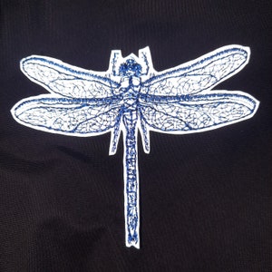 May include: A blue embroidered dragonfly with white outline on a black fabric background.
