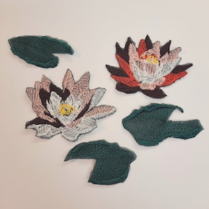 May include: Five embroidered iron-on patches featuring water lily flowers and leaves. The flowers are pink, white, red, and black. The leaves are green.