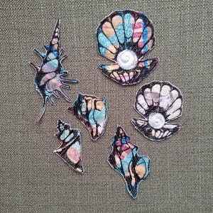 Puede incluir: Siete parches de tela bordados de colores con forma de conchas. Los parches son en tonos de azul, rosa, blanco y negro. Los parches son perfectos para añadir un toque de fantasía a la ropa, los bolsos u otras manualidades.