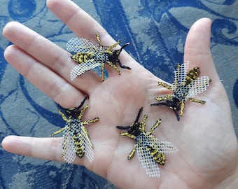 May include: Four embroidered yellow and black bee appliques with white mesh wings on a hand.