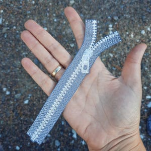 Può includere: Una cerniera grigia con denti bianchi. La cerniera è lunga circa 15 cm.