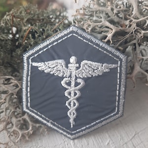 May include: A gray hexagonal patch with a white embroidered medical symbol, a snake wrapped around a staff with wings.