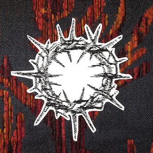 Può includere: Illustrazione in bianco e nero di una corona di spine con centro bianco. La corona è posta su uno sfondo strutturato blu scuro, rosso e arancione.