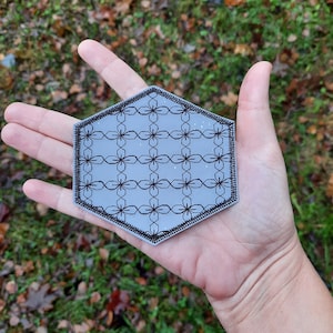 Peut inclure: Un dessous de verre hexagonal gris avec un motif géométrique noir et blanc. Le dessous de verre a une bordure décorative.