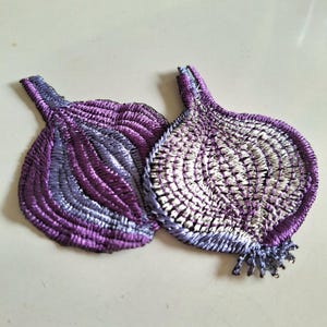May include: Two embroidered patches in the shape of an onion. The patches feature shades of purple, lavender, and white thread, with a detailed, textured appearance. The onion patches have a stem and root detail.