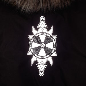 May include: A black jacket with a white reflective patch featuring a circular design with a cross inside. The patch is surrounded by a starburst pattern and a triangle.