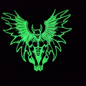 Könnte beinhalten: Grüner, im Dunkeln leuchtender gestickter Aufnäher eines geflügelten Dämons mit muskulösem Körperbau, der mit ausgebreiteten Flügeln sitzt.