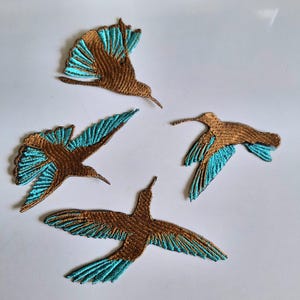 Può includere: Quattro toppe ricamate a forma di colibrì in volo. Ogni toppa presenta un corpo e ali color bronzo metallizzato con accenti di filo blu turchese brillante sulle punte delle ali e sulle piume della coda, con cuciture dettagliate.