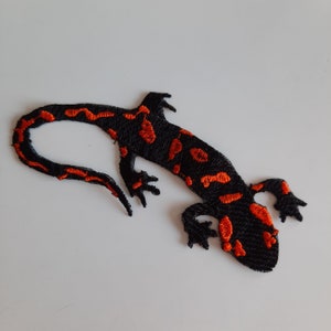 Pu&ograve; includere: Toppa ricamata nera e arancione di una salamandra con un design dettagliato.