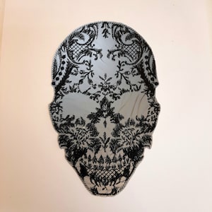 May include: A black and white skull design with a lace pattern. The skull is outlined in black and the lace pattern is filled in with black.