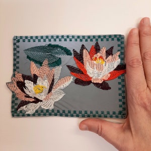 Pode incluir: Um remendo de tecido cinza com uma borda verde e flores bordadas de rosa, branco e vermelho.