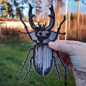 May include: A black and white embroidered iron-on patch of a stag beetle with detailed markings.