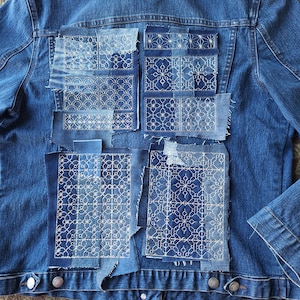 May include: A denim jacket with multiple patches sewn on the back. The patches are made of blue denim and feature white embroidery in geometric patterns.