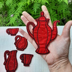 Könnte beinhalten: Rotes Filz-Applikations-Tee-Set mit Teekanne, Milchkännchen, Zuckerdose und zwei Tassen. Das Set ist handgenäht und hat ein Punkte-Muster.