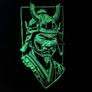 Op de afbeelding: Een neon groen geborduurd ontwerp van een samoerai krijger op een zwarte achtergrond. De samoerai draagt een helm met hoorns en een gedetailleerd gezichtsmasker. Het ontwerp is ingesloten in een rechthoekig frame.