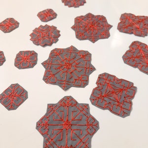 Könnte beinhalten: Eine Sammlung grauer Filz-Schneeflocken-Ornamente mit roter Stickerei. Die Schneeflocken sind in verschiedenen Größen und Formen.