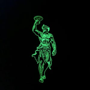 Puede incluir: Un parche bordado verde que brilla en la oscuridad que representa a un hombre sosteniendo una antorcha, posiblemente un dios griego.