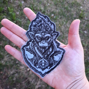 May include: Black and white embroidered patch of a monkey with a crown and a fierce expression.