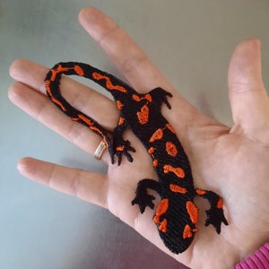 Pu&ograve; includere: Toppa ricamata nera e arancione di una salamandra con la coda arricciata.
