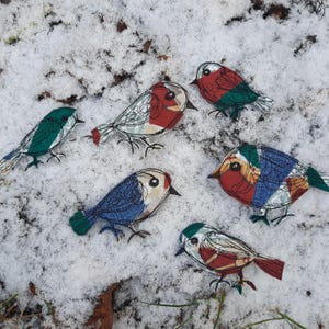 Op de afbeelding: Vijf kleurrijke stoffen vogelversieringen met geborduurde details. De vogels staan in verschillende poses en hebben verschillende patronen en kleuren, waaronder rood, blauw, groen en wit.