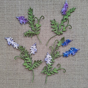 May include: Embroidered floral design on a beige linen fabric. The design features multiple sprigs of green leaves with purple and blue flowers.