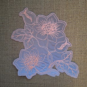 Peut inclure: Un patch brodé bleu clair avec un motif floral rose. Le patch présente deux grandes fleurs avec de multiples pétales et feuilles.