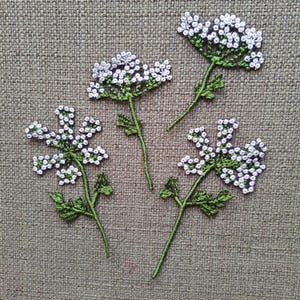 Könnte beinhalten: Vier gestickte weiße Blumen mit grünen Stielen auf braunem Leinen Hintergrund.