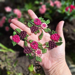 Könnte beinhalten: Gestickte Blumenapplikationen in Fuchsia, Burgunderrot und Hellrosa mit grünen Blättern. Die Applikationen sind auf einer Hand angeordnet und zeigen die Details der Stickerei. Diese dekorativen Applikationen sind ideal zum Verzieren von Kleidung oder Bastelprojekten.