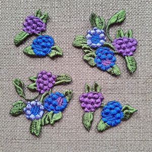 May include: Four embroidered fabric appliques featuring clusters of purple, blue, and green flowers. The appliques are perfect for adding a touch of floral charm to crafts and sewing projects.