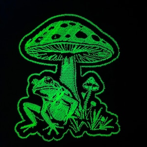 May include: A green glow-in-the-dark embroidered patch featuring a mushroom with a frog sitting under it.
