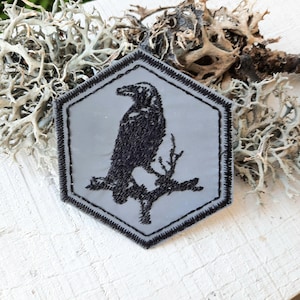 Peut inclure: Un corbeau brodé noir perché sur une branche, sur un patch hexagonal gris.