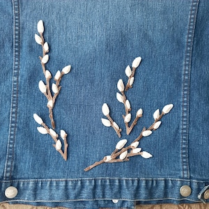 Könnte beinhalten: Eine Jeansjacke mit drei gestickten weißen und braunen Weidenzweigen.