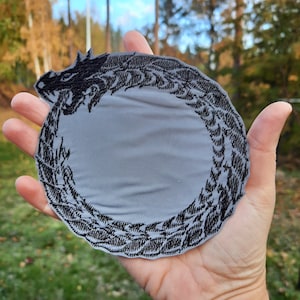 May include: A black embroidered patch of a dragon curled in a circle, on a gray background.